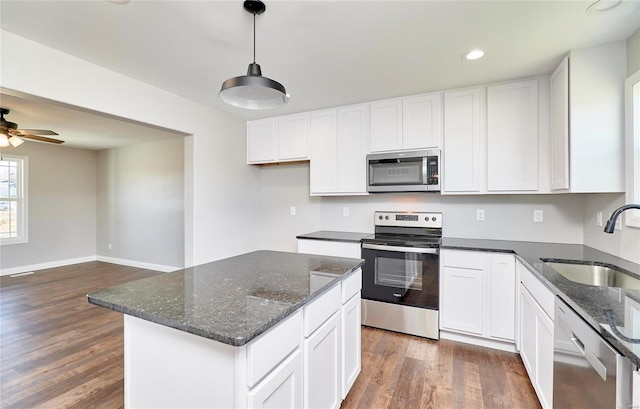 kitchen with stainless steel appliances, dark wood-type flooring, a sink, white cabinets, and dark stone counters