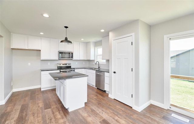 kitchen featuring baseboards, white cabinets, dark countertops, appliances with stainless steel finishes, and a center island