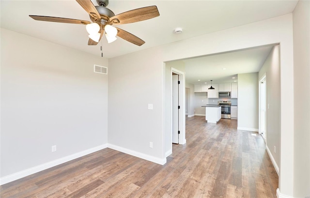 empty room with a ceiling fan, wood finished floors, visible vents, and baseboards