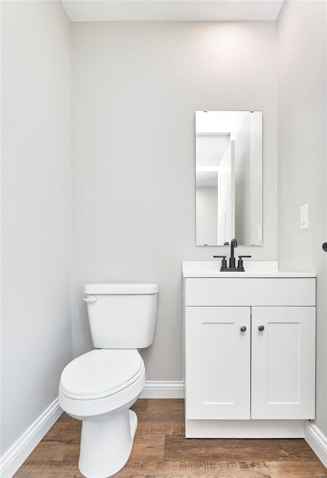 half bath with toilet, baseboards, wood finished floors, and vanity