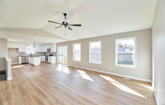 unfurnished living room featuring vaulted ceiling, ceiling fan, sink, and light wood-type flooring