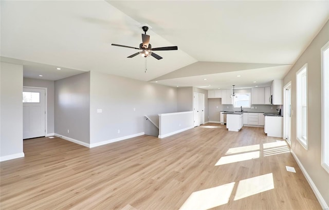 unfurnished living room with ceiling fan, sink, vaulted ceiling, and light hardwood / wood-style flooring