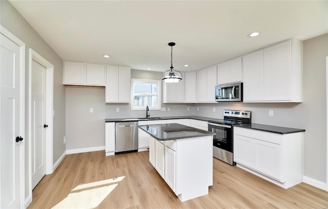 kitchen with appliances with stainless steel finishes, sink, white cabinets, light hardwood / wood-style floors, and a kitchen island