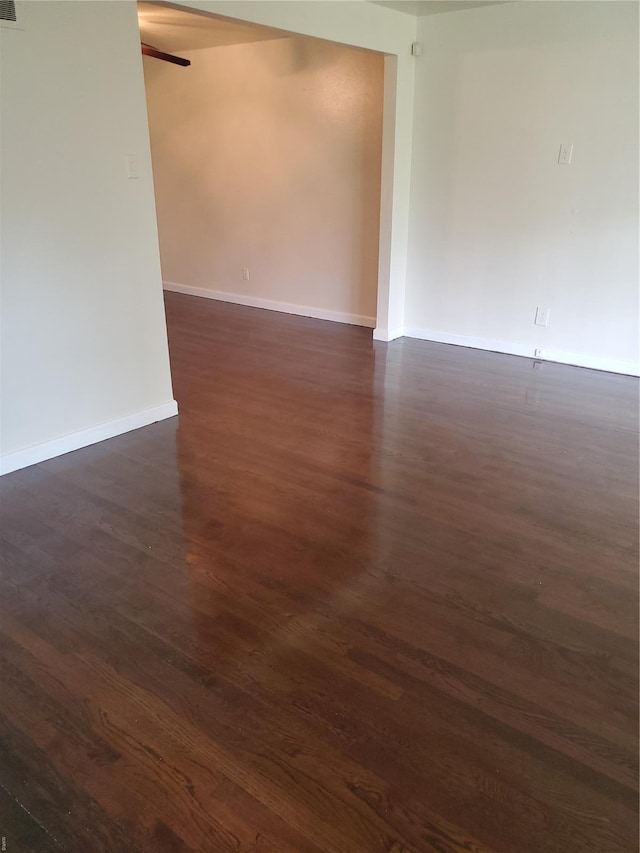 spare room featuring baseboards, a ceiling fan, and dark wood finished floors