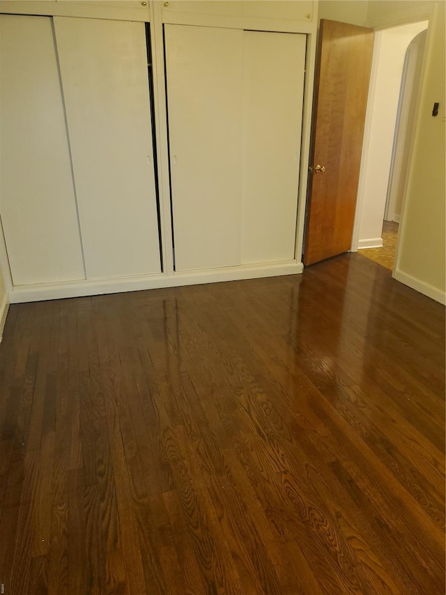unfurnished bedroom with arched walkways, baseboards, and dark wood-type flooring