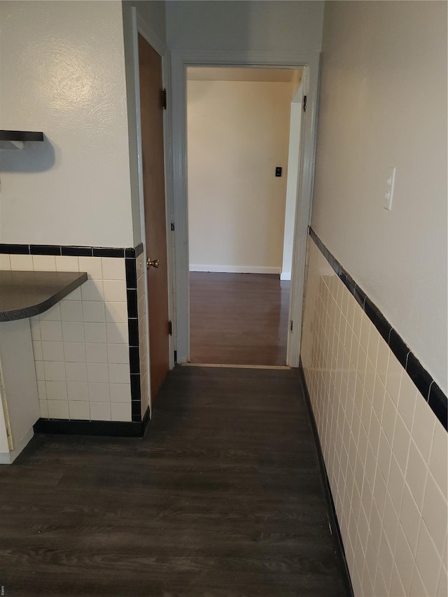 hall featuring tile walls, wainscoting, and dark wood-style floors