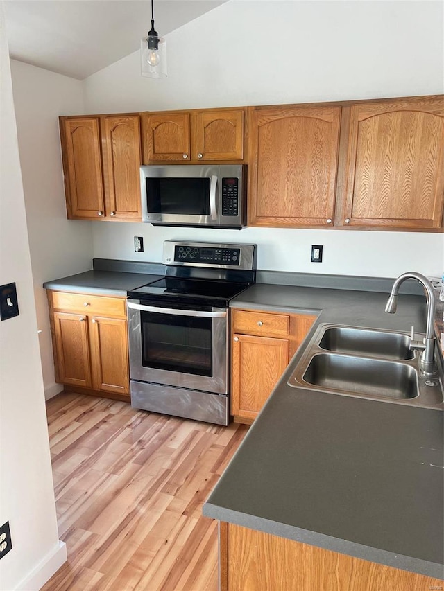 kitchen with sink, light hardwood / wood-style floors, vaulted ceiling, appliances with stainless steel finishes, and decorative light fixtures