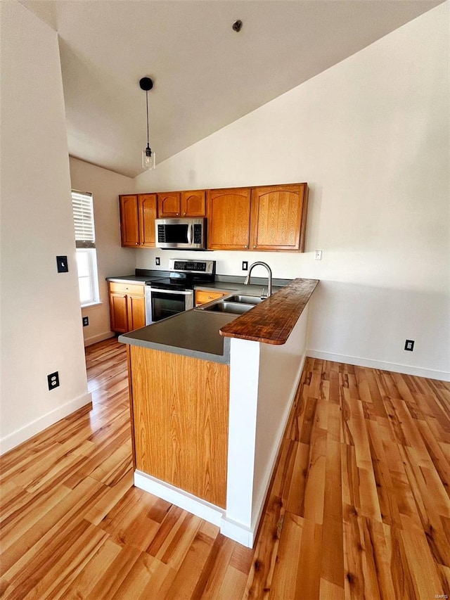 kitchen with lofted ceiling, light hardwood / wood-style floors, pendant lighting, kitchen peninsula, and appliances with stainless steel finishes