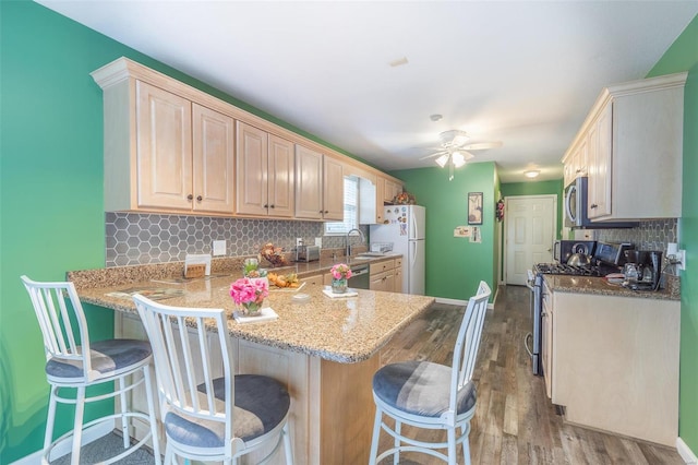 kitchen with a breakfast bar, kitchen peninsula, stainless steel appliances, wood-type flooring, and ceiling fan