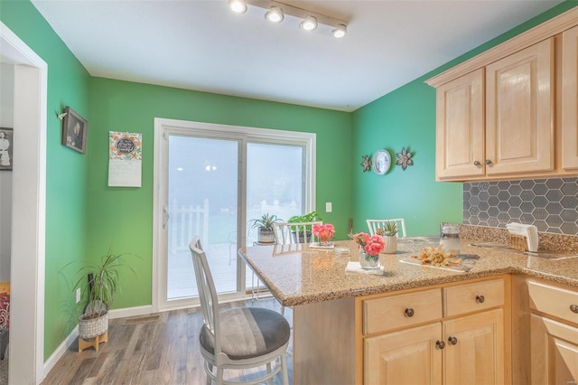 kitchen featuring tasteful backsplash, kitchen peninsula, a breakfast bar area, light brown cabinetry, and hardwood / wood-style flooring