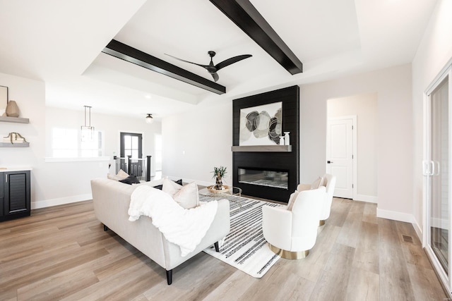 living room featuring a large fireplace, ceiling fan, beamed ceiling, and light wood-type flooring