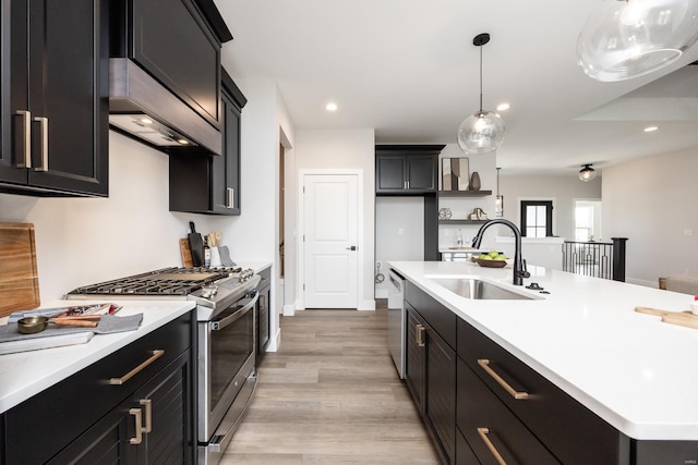 kitchen with pendant lighting, light wood-type flooring, sink, an island with sink, and appliances with stainless steel finishes