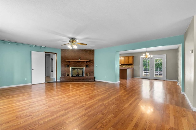 unfurnished living room with light wood-type flooring, ceiling fan with notable chandelier, a textured ceiling, and a brick fireplace