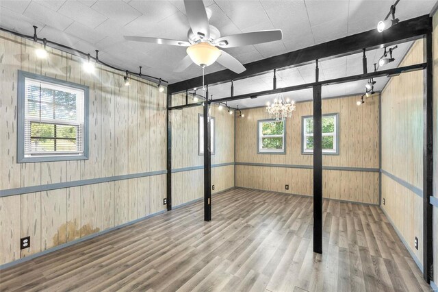 basement featuring hardwood / wood-style flooring, ceiling fan with notable chandelier, and wooden walls