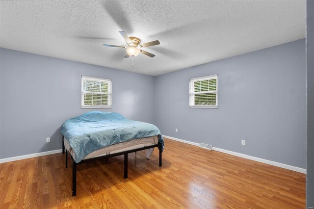 bedroom featuring ceiling fan, a textured ceiling, light hardwood / wood-style floors, and multiple windows