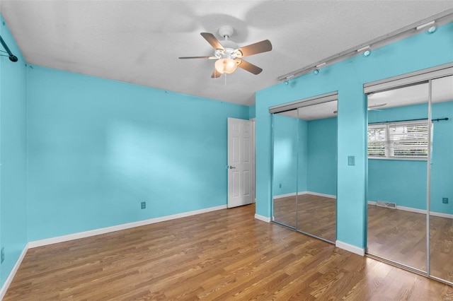 unfurnished bedroom featuring a textured ceiling, hardwood / wood-style floors, ceiling fan, track lighting, and two closets