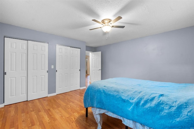 bedroom featuring ceiling fan, hardwood / wood-style flooring, two closets, and a textured ceiling