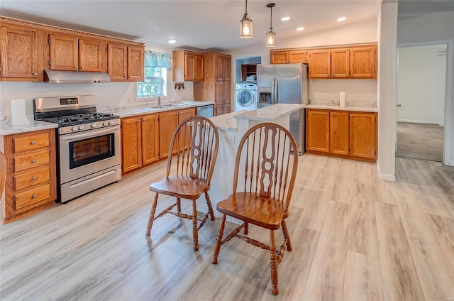 kitchen with light wood-type flooring, washer / clothes dryer, vaulted ceiling, hanging light fixtures, and stainless steel appliances