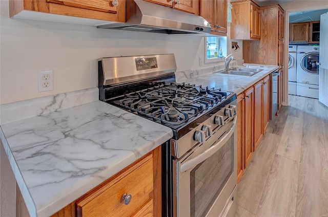 kitchen with appliances with stainless steel finishes, light hardwood / wood-style floors, separate washer and dryer, light stone countertops, and sink