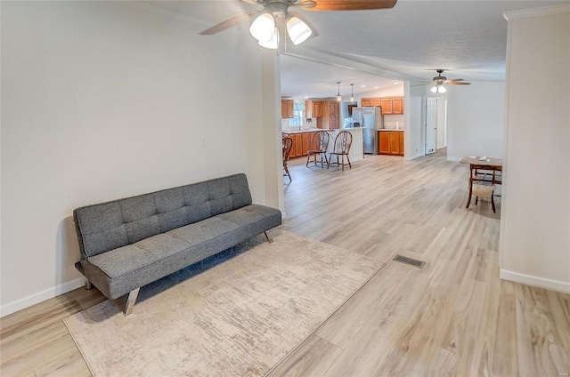 living area with ceiling fan, a textured ceiling, light wood-type flooring, and ornamental molding