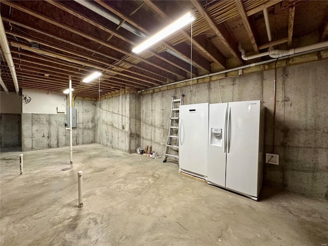 basement featuring white refrigerator with ice dispenser, electric panel, and white fridge