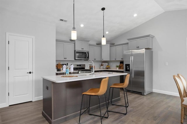 kitchen with a kitchen breakfast bar, appliances with stainless steel finishes, vaulted ceiling, and dark hardwood / wood-style flooring