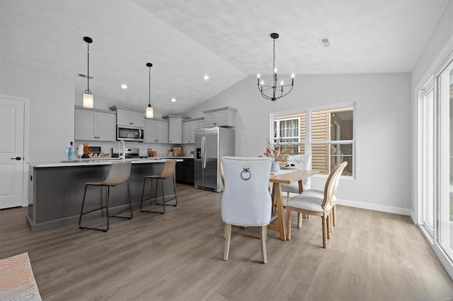 dining space featuring an inviting chandelier, lofted ceiling, light wood-type flooring, and a healthy amount of sunlight