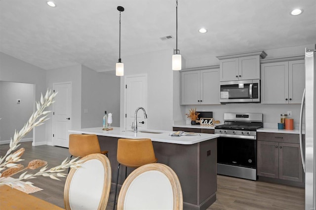 kitchen featuring dark hardwood / wood-style flooring, pendant lighting, stainless steel appliances, a center island with sink, and sink