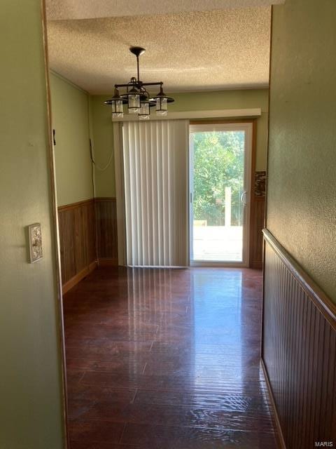 spare room featuring wooden walls, a chandelier, a textured ceiling, and hardwood / wood-style flooring