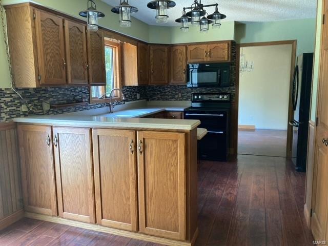 kitchen featuring a notable chandelier, dark hardwood / wood-style floors, kitchen peninsula, and black appliances