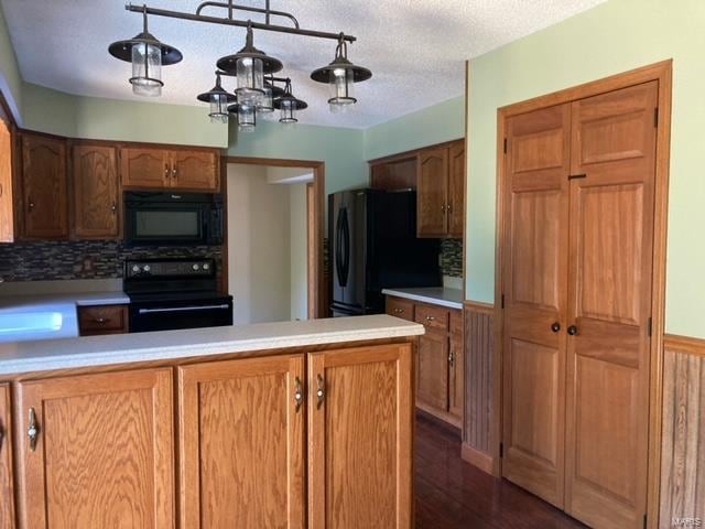 kitchen featuring dark wood-type flooring, kitchen peninsula, hanging light fixtures, decorative backsplash, and black appliances