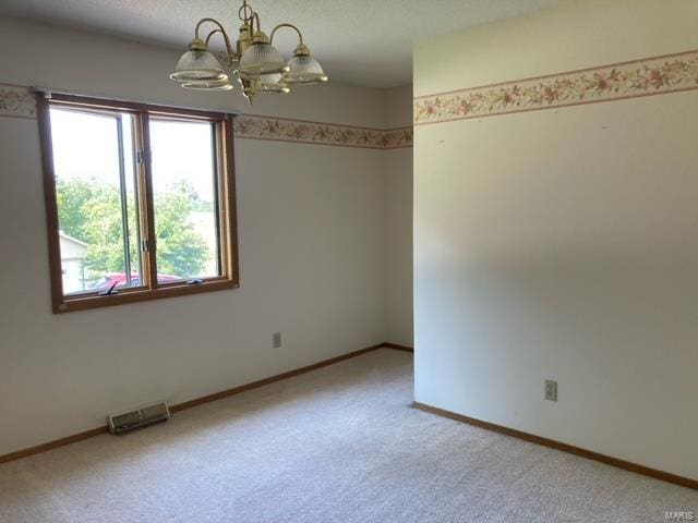 spare room featuring light colored carpet, a textured ceiling, and a chandelier