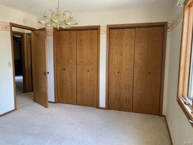 unfurnished bedroom featuring an inviting chandelier, light carpet, and multiple closets