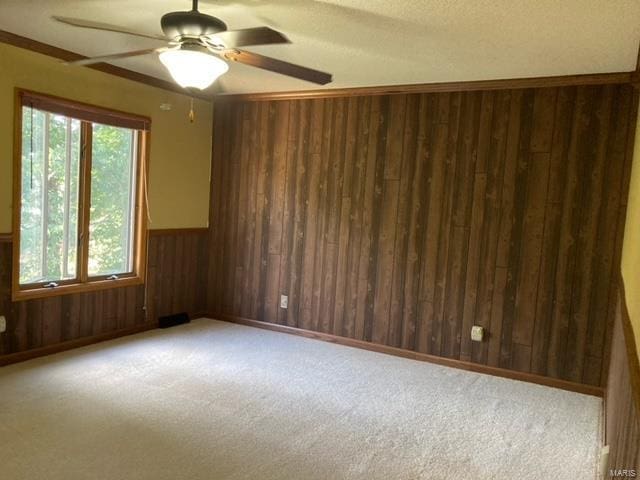 carpeted spare room featuring wood walls, ceiling fan, and a textured ceiling