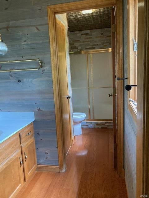 bathroom with hardwood / wood-style flooring, wood walls, walk in shower, vanity, and toilet