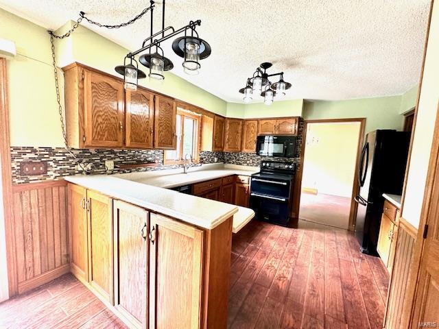 kitchen with black appliances, kitchen peninsula, hanging light fixtures, and hardwood / wood-style floors