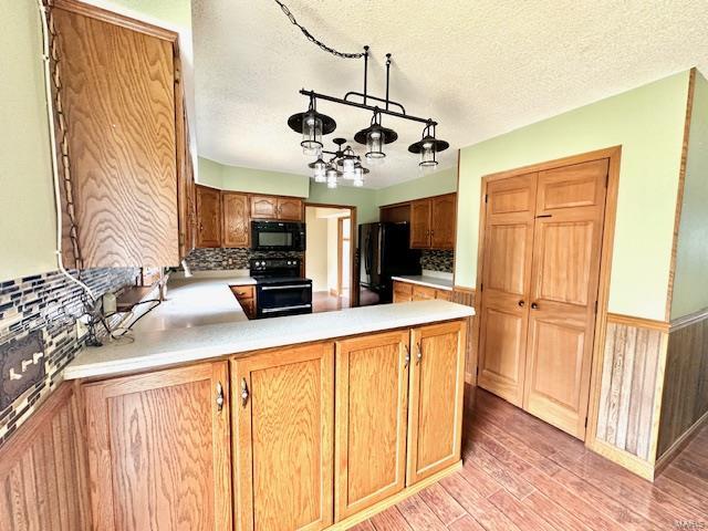 kitchen with decorative backsplash, kitchen peninsula, a textured ceiling, black appliances, and light wood-type flooring