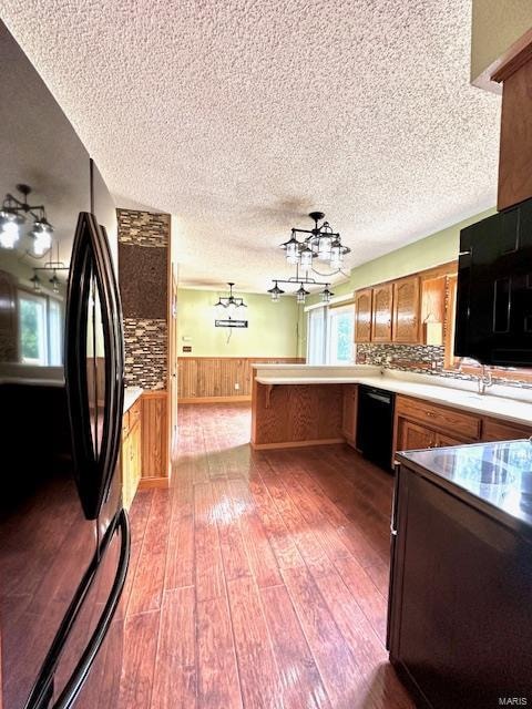 kitchen with wood walls, kitchen peninsula, a textured ceiling, light hardwood / wood-style flooring, and black appliances