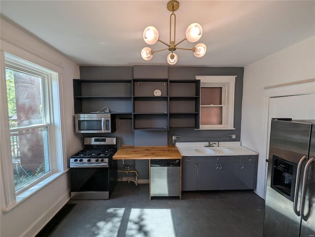 kitchen with a chandelier, sink, butcher block counters, hanging light fixtures, and appliances with stainless steel finishes