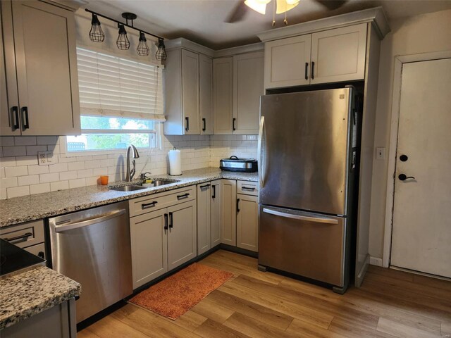 kitchen with light wood-type flooring, sink, tasteful backsplash, stainless steel appliances, and light stone countertops