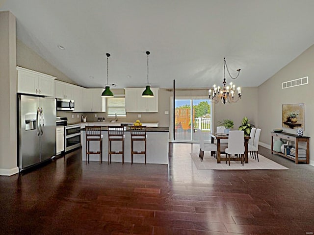 kitchen featuring dark wood-type flooring, stainless steel appliances, a center island, decorative light fixtures, and white cabinetry