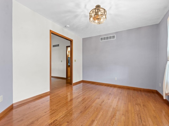 unfurnished room featuring an inviting chandelier and light wood-type flooring