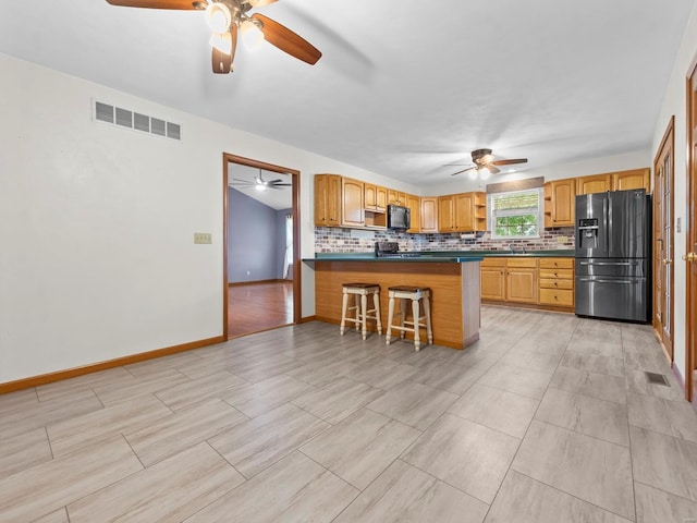 kitchen featuring a breakfast bar area, kitchen peninsula, decorative backsplash, and stainless steel refrigerator with ice dispenser