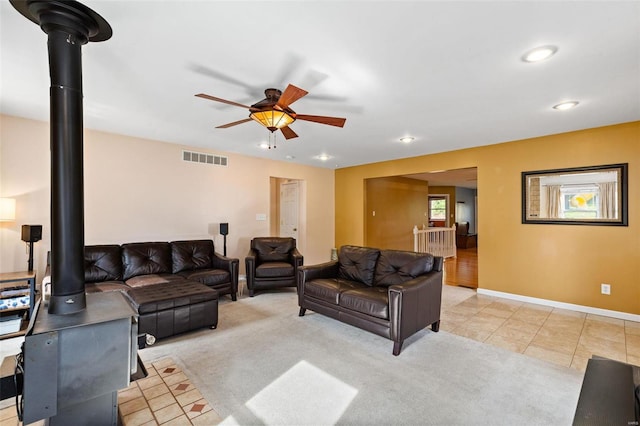 tiled living room featuring a wood stove and ceiling fan