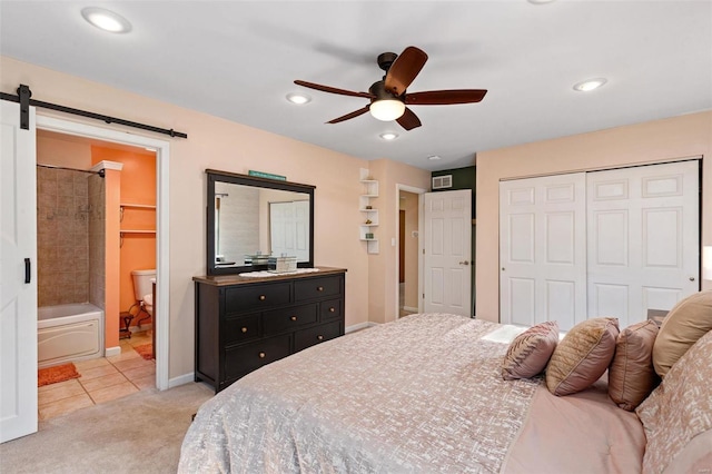 bedroom with ceiling fan, a barn door, a closet, ensuite bath, and light colored carpet