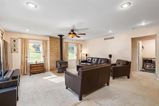 living room featuring light carpet, a wood stove, and ceiling fan