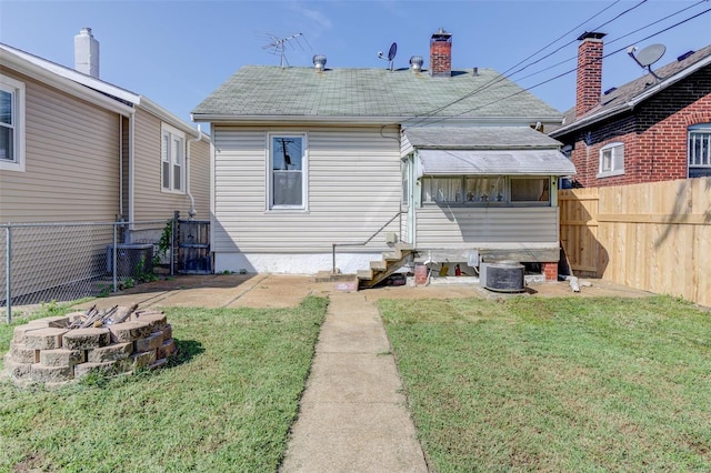 back of property featuring a lawn, central air condition unit, and a fire pit