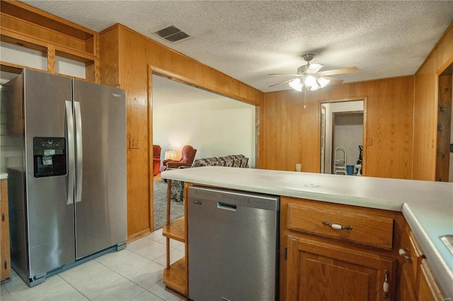 kitchen featuring wooden walls, ceiling fan, appliances with stainless steel finishes, and a textured ceiling