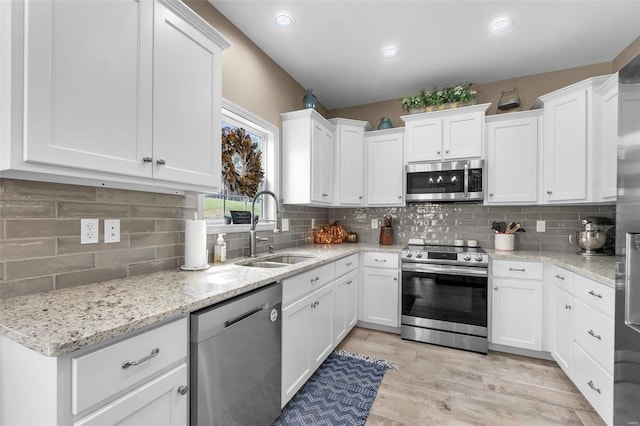 kitchen with appliances with stainless steel finishes, decorative backsplash, white cabinets, light wood-type flooring, and sink