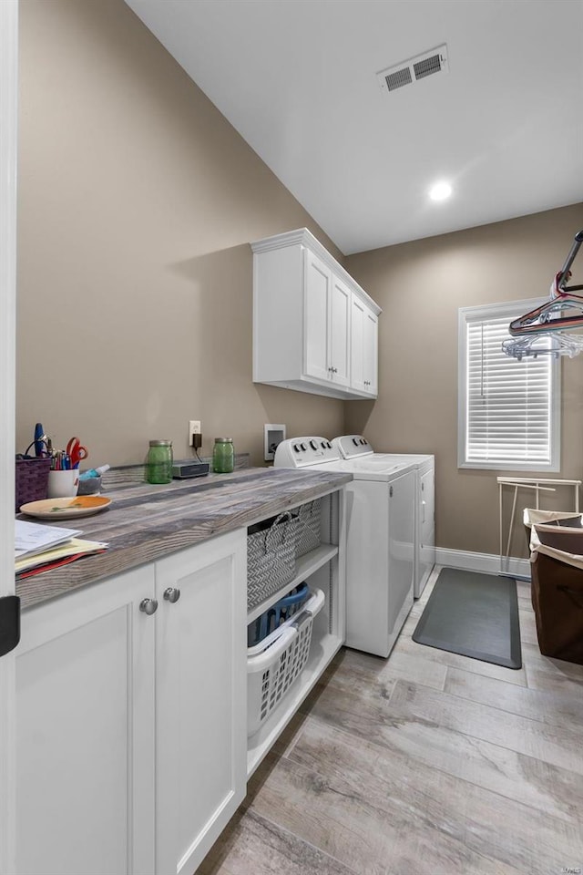 clothes washing area featuring light hardwood / wood-style flooring, washing machine and clothes dryer, and cabinets